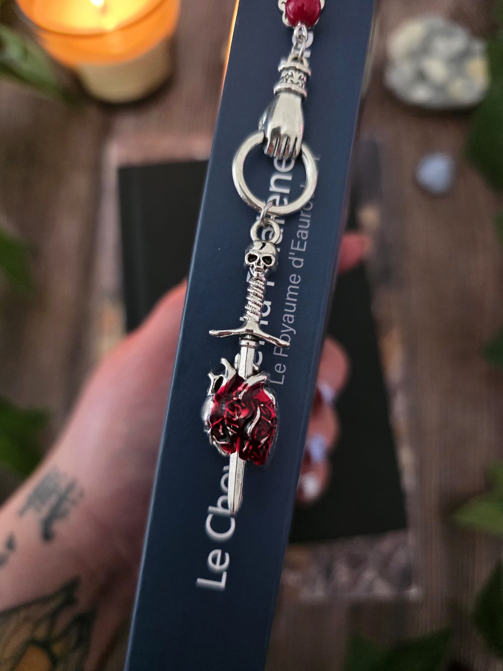 Marque-page "Le voeu de l'épée", un coeur humain transpercé par une épée, avec une breloque main au dessus qui tient l'épée ainsi qu'une pierre naturelle de corail rouge. Le signet est en métal et évoque un bijou de livre très beau pour les romans de fantasy, dark fantasy et romantasy. dans un livre