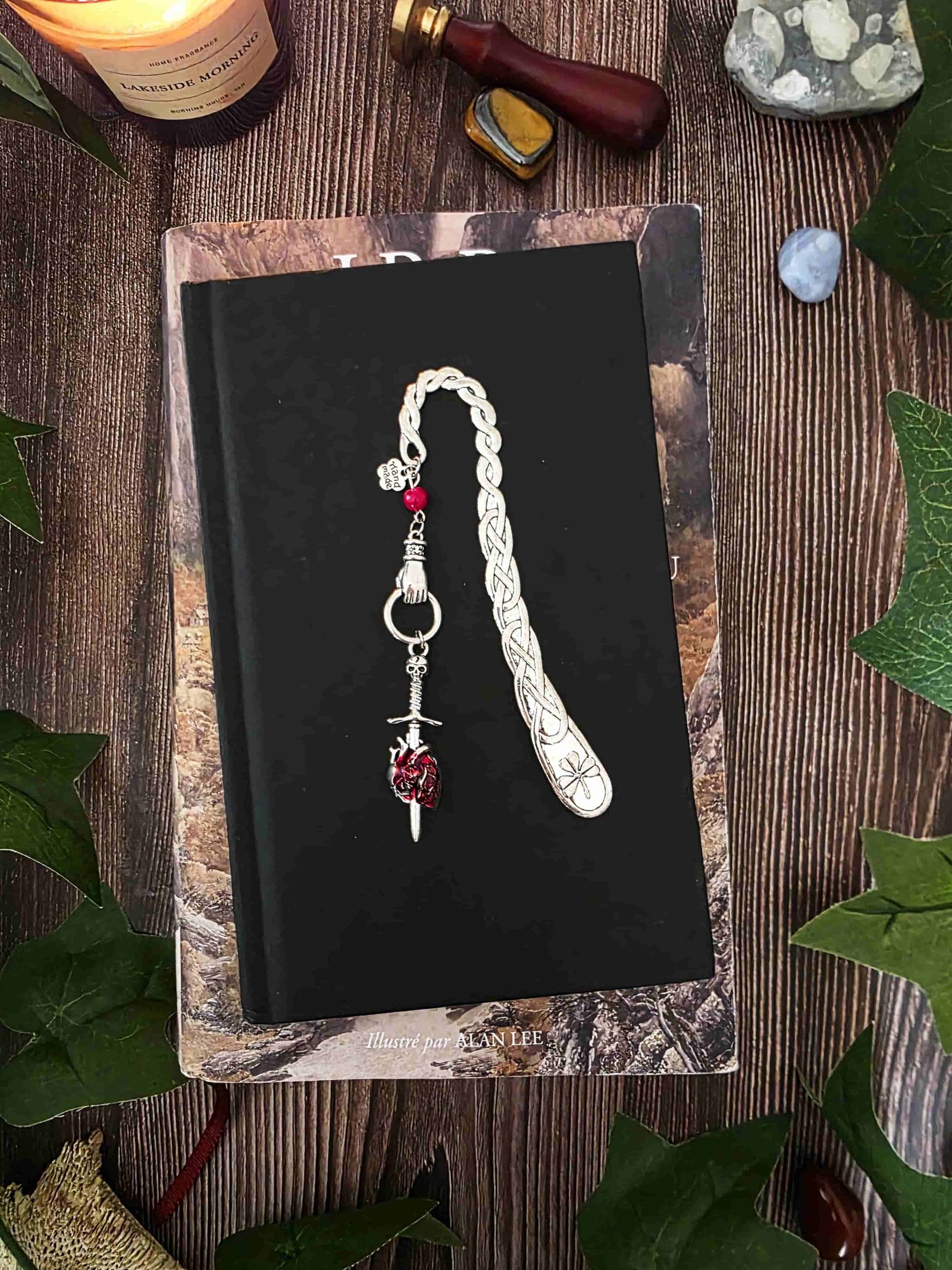 Marque-page "Le voeu de l'épée", un coeur humain transpercé par une épée, avec une breloque main au dessus qui tient l'épée ainsi qu'une pierre naturelle de corail rouge. Le signet est en métal et évoque un bijou de livre très beau pour les romans de fantasy, dark fantasy et romantasy
