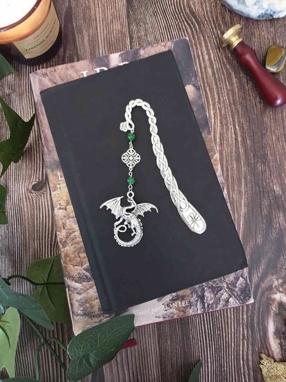 Marque-page en métal Dragon orné de pierres fines naturelles de jade, personnalisable. Le signet est posé sur un livre noir, un livre de Tolkien en dessous. 