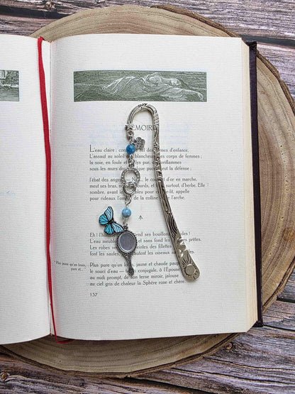 marque-page miroir enchanté, papillon bleu avec un ruban et deux pierres naturelles d'apatite bleue. Le signet est fait à la main par bellette workshop. Ce bijou de lecture est personnalisable. vu dans les pages d'un livre